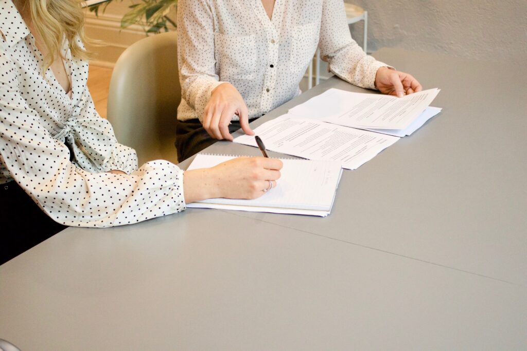 Image illustrative pour une consultations : deux personnes assises autour d'une table, l'une commente des documents, l'autre prend des notes.